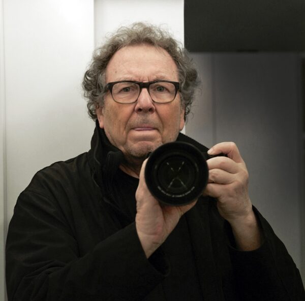 Mann mittleren Alters mit Brille hält eine Kamera vor dem Gesicht, als würde er ein Foto machen.